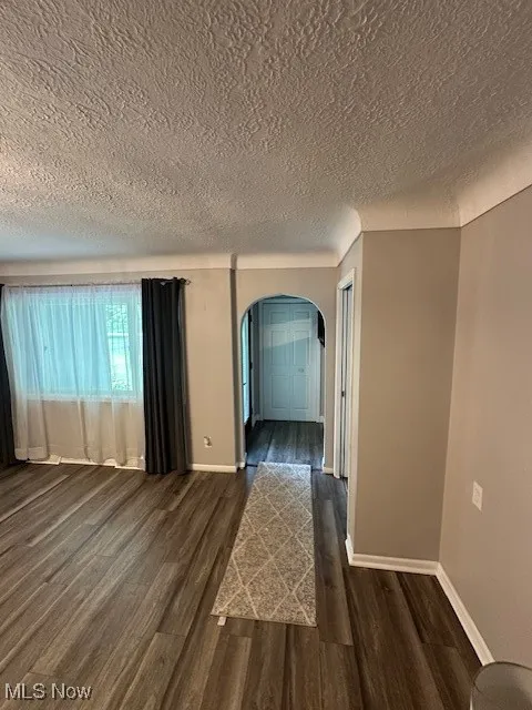 Unfurnished room featuring arched walkways, a textured ceiling, and dark wood-style floors