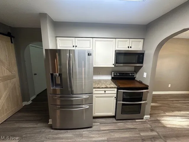 Kitchen featuring fridge, range, arched walkways, and white cabinetry