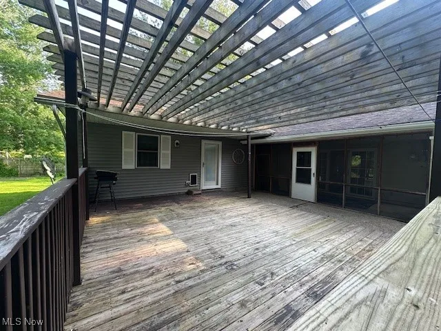 Wooden deck featuring a pergola and a sunroom