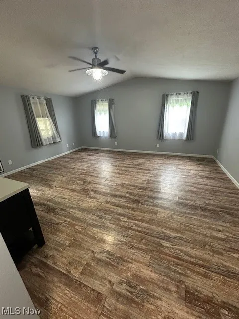 Unfurnished living room featuring vaulted ceiling, dark wood-style floors, healthy amount of natural light, a ceiling fan, and a textured ceiling