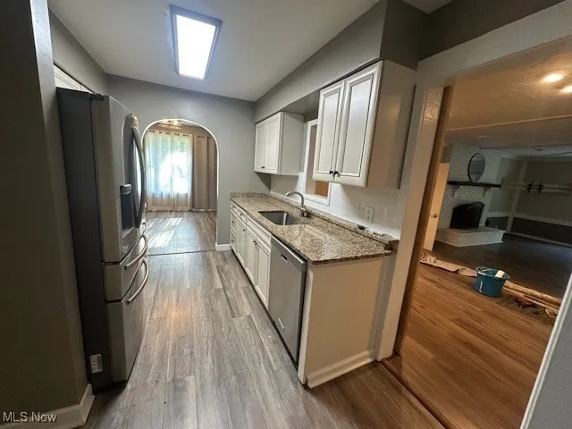 Kitchen featuring refrigerator, dishwashing machine, arched walkways, light stone countertops, and white cabinetry