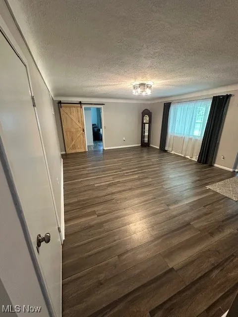 Unfurnished room with a textured ceiling, dark wood finished floors, a barn door, and arched walkways