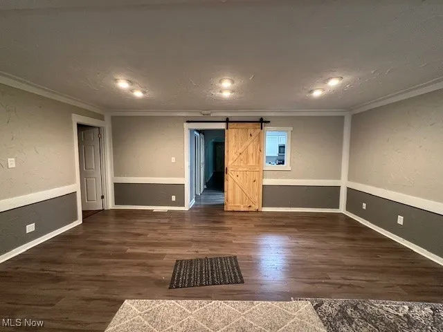 Empty room with ornamental molding, a barn door, wood finished floors, and a textured wall