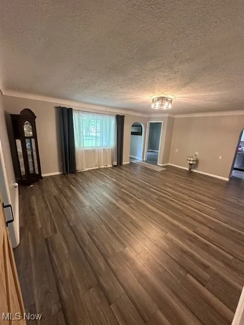 Unfurnished living room featuring arched walkways, a textured ceiling, and dark wood-style flooring