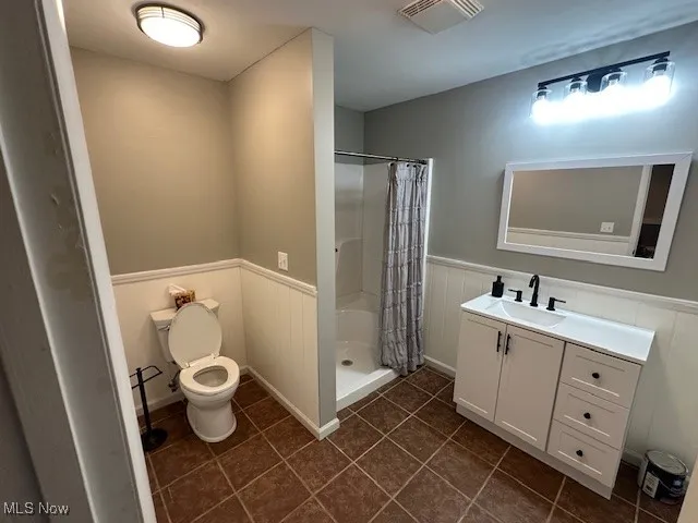 Bathroom featuring vanity, a wainscoted wall, tile patterned flooring, and a shower stall