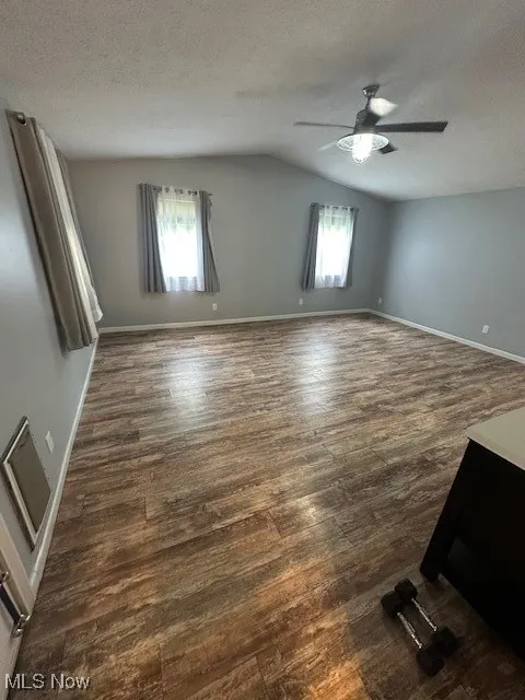 Spare room with a ceiling fan, vaulted ceiling, dark wood-style floors, a textured ceiling, and healthy amount of natural light