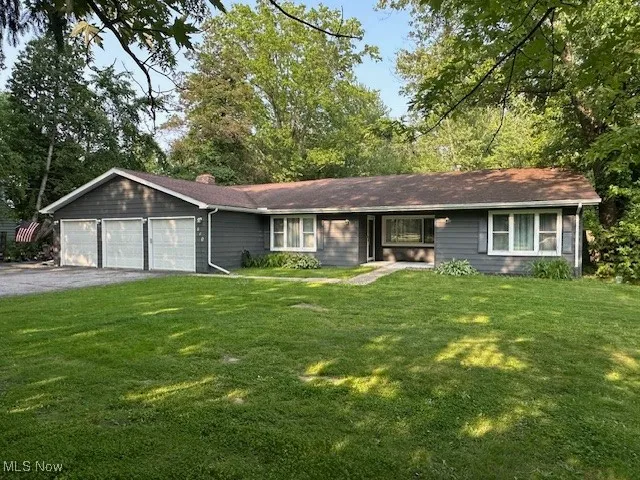 Ranch-style home featuring an attached garage, asphalt driveway, a front yard, and a chimney