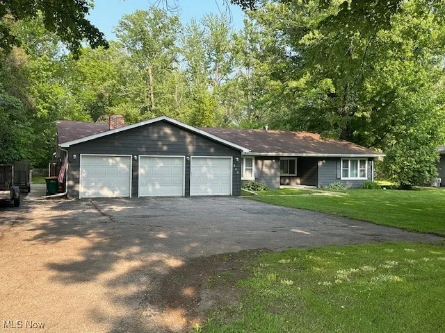 Ranch-style house with driveway, a front lawn, a chimney, and an attached garage