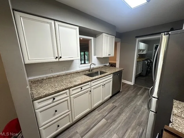 Kitchen featuring fridge, dishwasher, dark wood-style flooring, white cabinetry, and light stone counters
