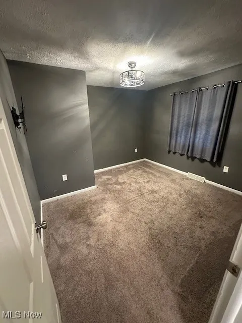 Unfurnished room with a textured ceiling and carpet flooring