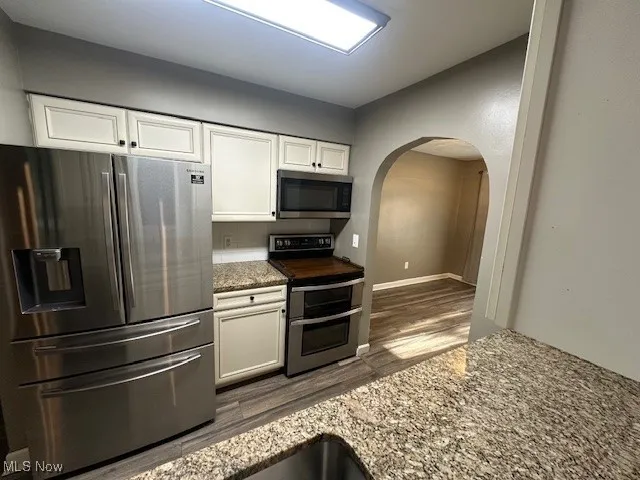 Kitchen with freestanding refrigerator, range, arched walkways, dark wood-type flooring, and white cabinetry