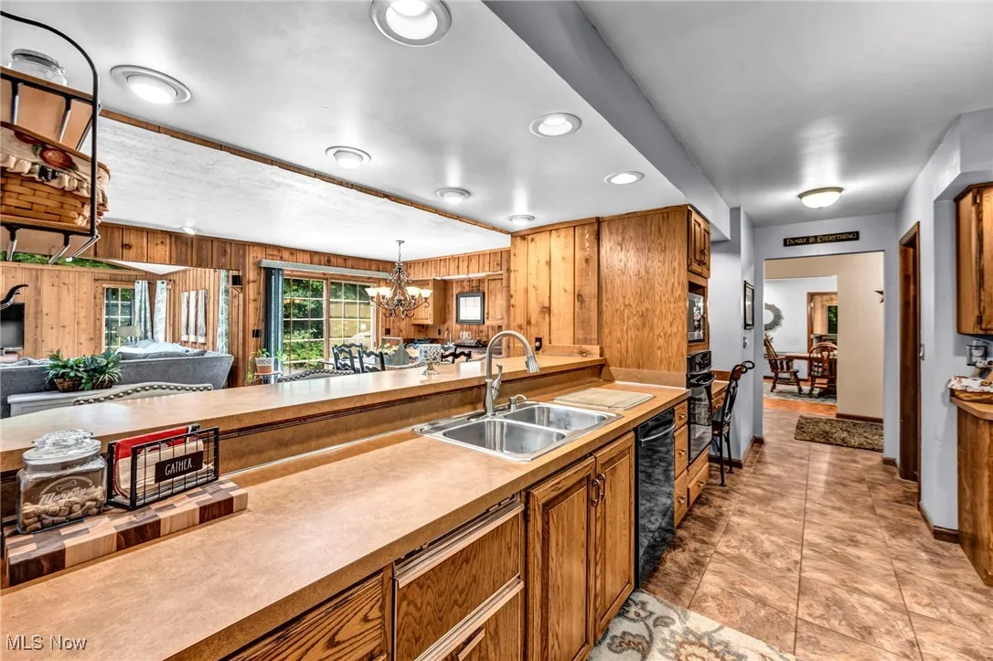Kitchen with a chandelier, wood walls, brown cabinetry, pendant lighting, and open floor plan