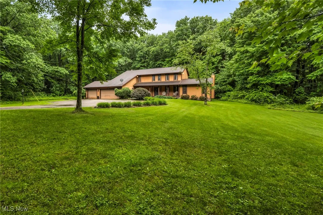 View of front of property with driveway, an attached garage, a front lawn, and a wooded view