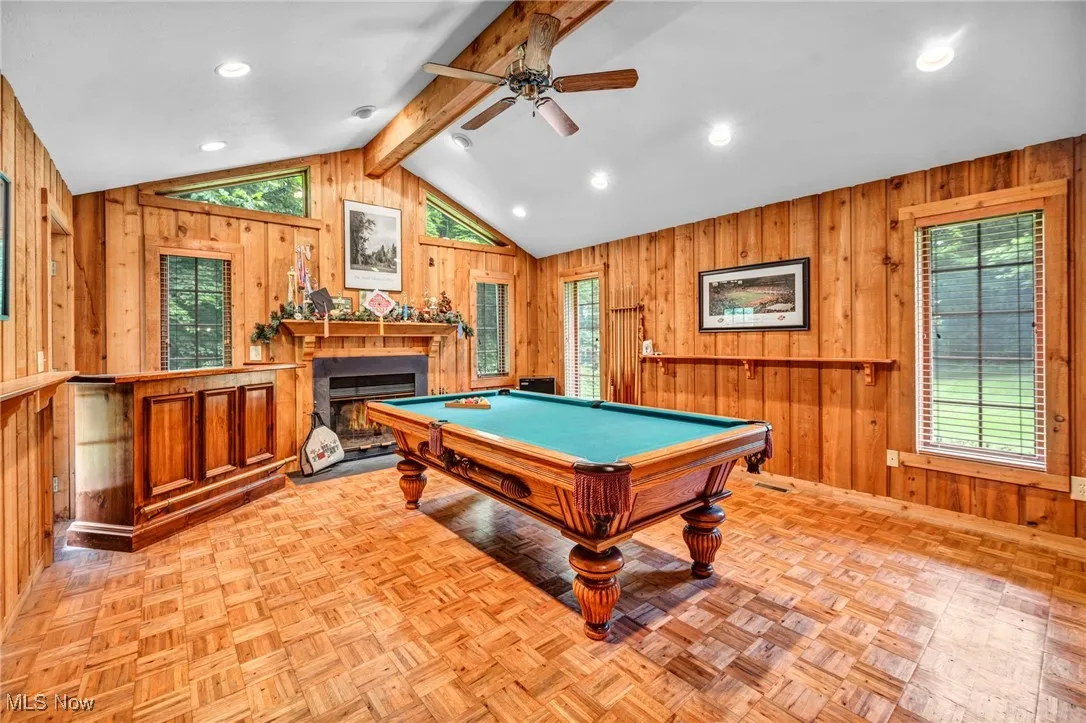 Rec room featuring wood walls, a ceiling fan, healthy amount of natural light, a warm lit fireplace, and billiards