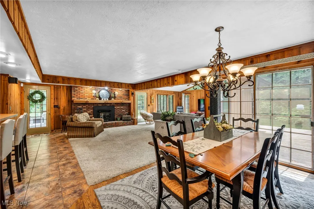 Dining space with wood walls, plenty of natural light, a chandelier, a textured ceiling, and a brick fireplace