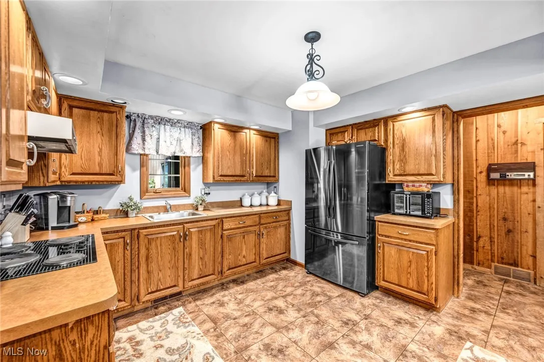 Kitchen featuring freestanding refrigerator, extractor fan, black electric cooktop, light countertops, and brown cabinets