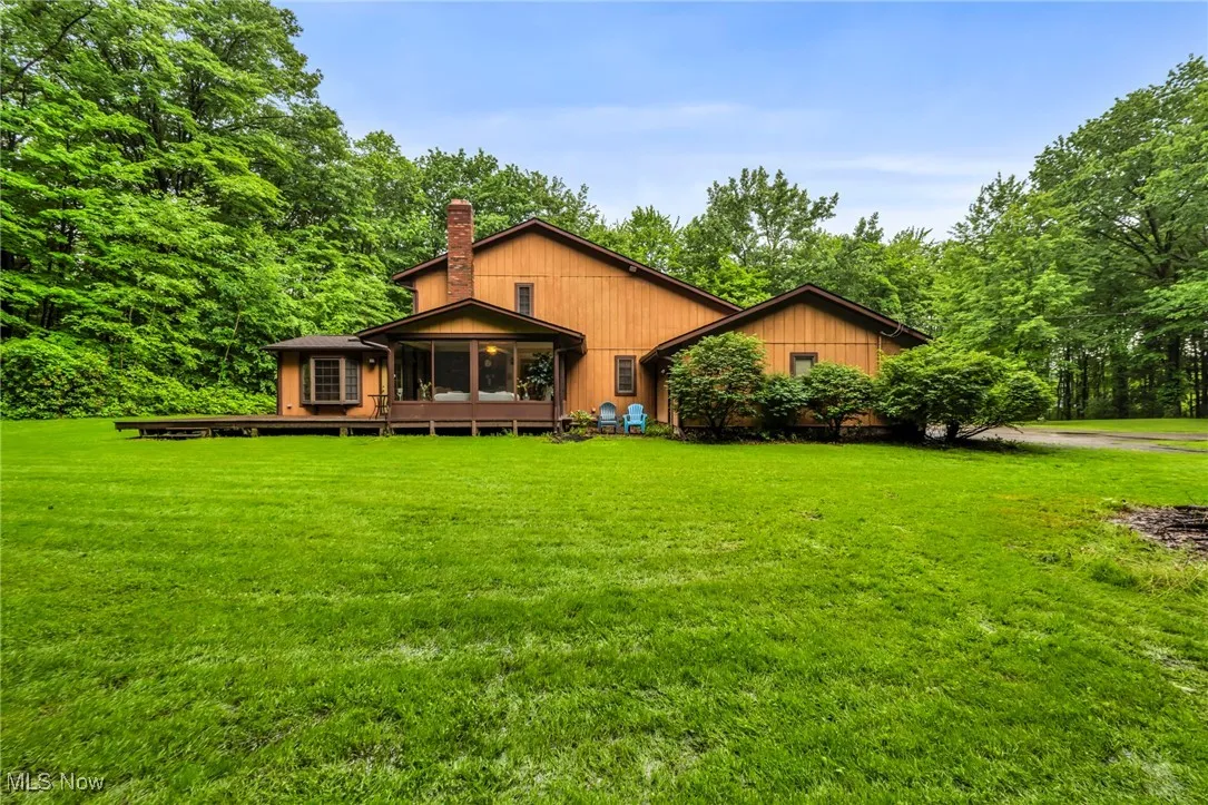 Back of property featuring a sunroom, a chimney, and a lawn