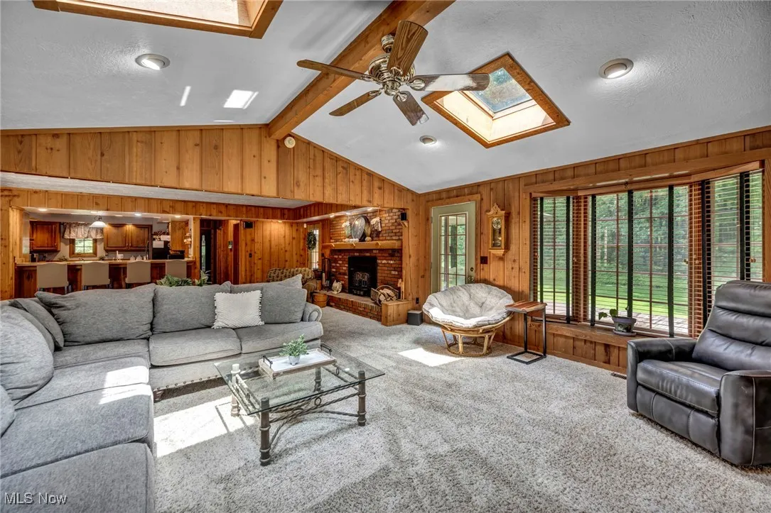 Carpeted living area featuring a skylight, wooden walls, a ceiling fan, and a fireplace