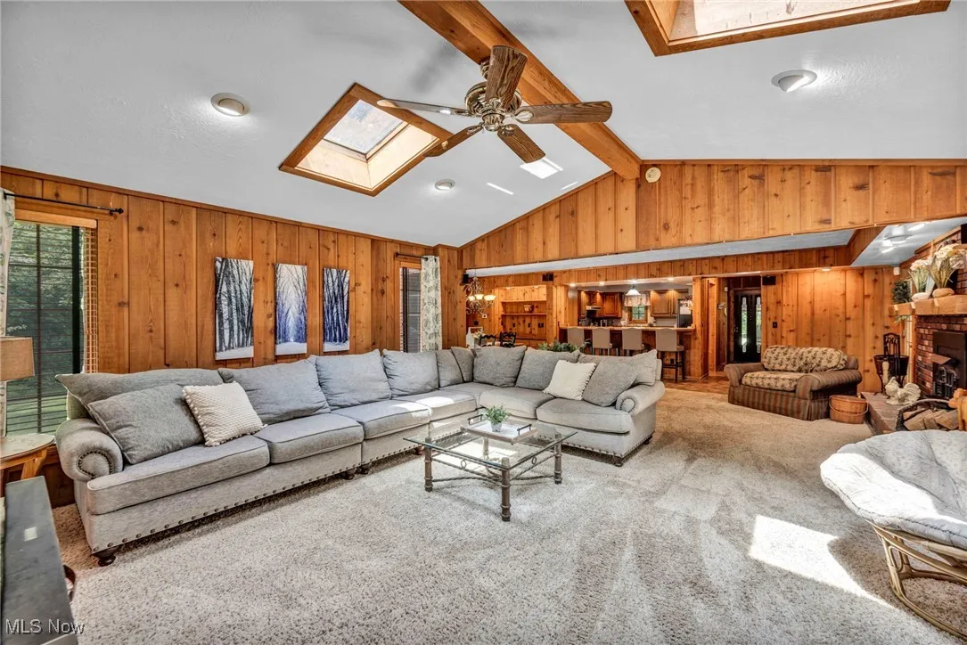 Living room featuring a skylight, wood walls, a ceiling fan, and carpet