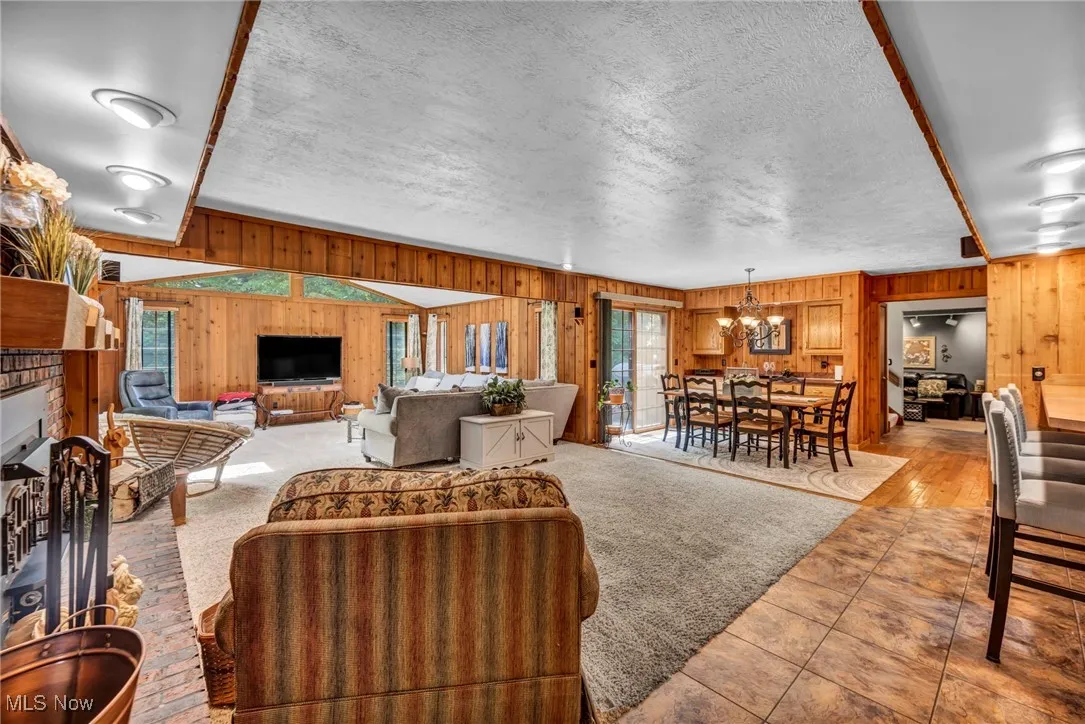 Tiled living area featuring wood walls, a chandelier, a brick fireplace, and a textured ceiling