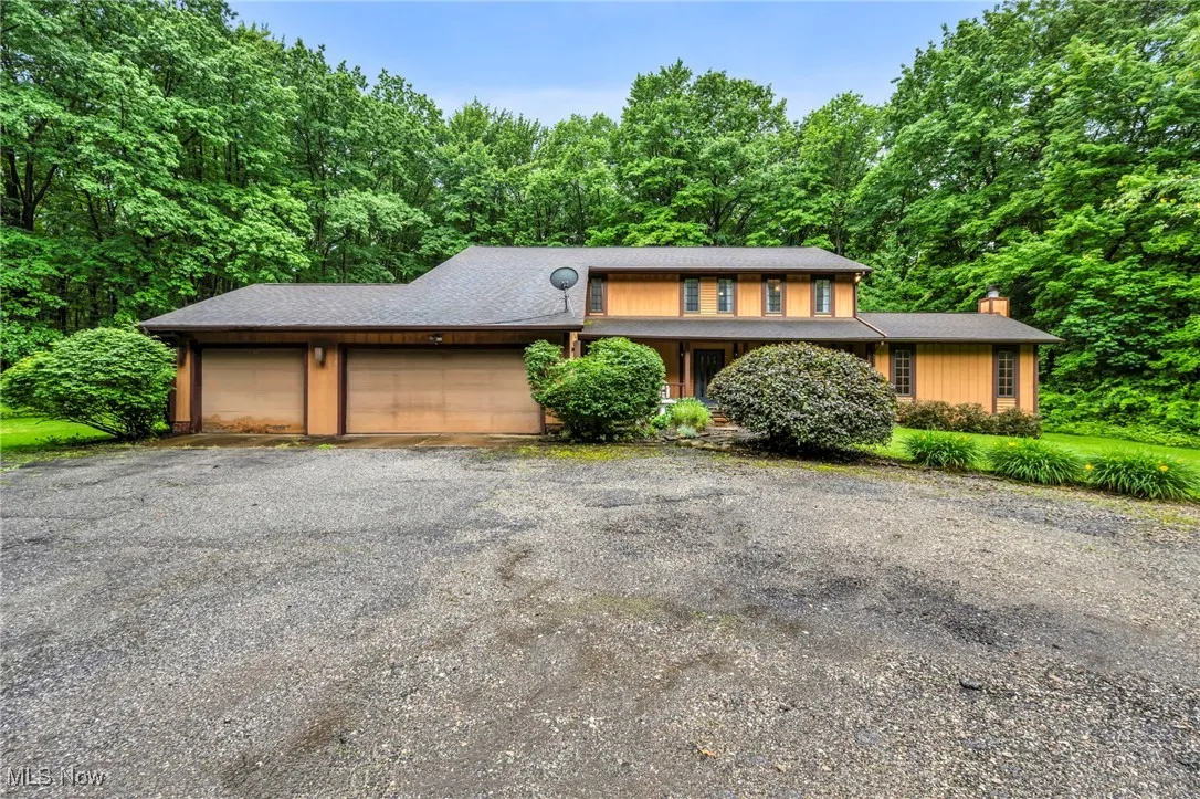 View of front of property with a garage, a chimney, driveway, and a view of trees