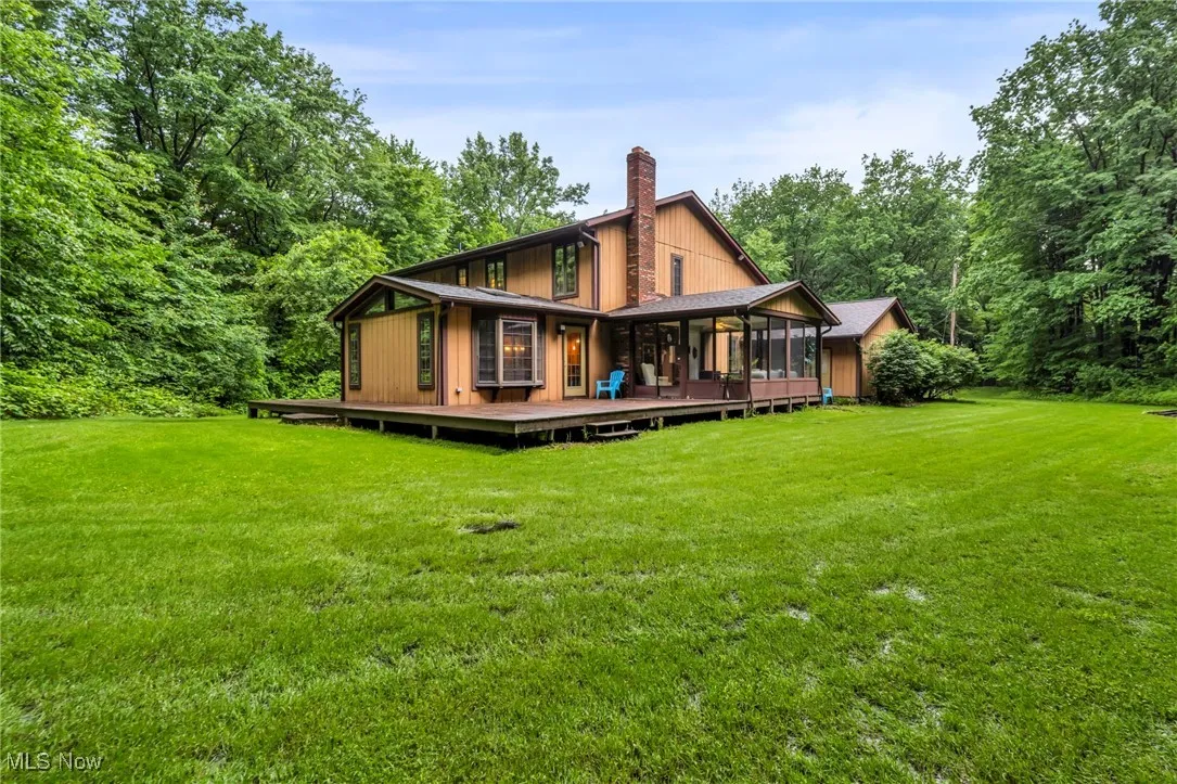 Rear view of property with a chimney, a lawn, a wooden deck, and a sunroom