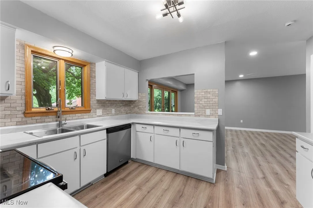 Kitchen with stainless steel dishwasher, light wood finished floors, and light countertops