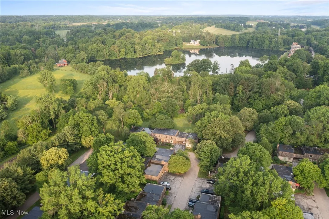 Aerial view of property and surrounding area featuring a nearby body of water and a heavily wooded area