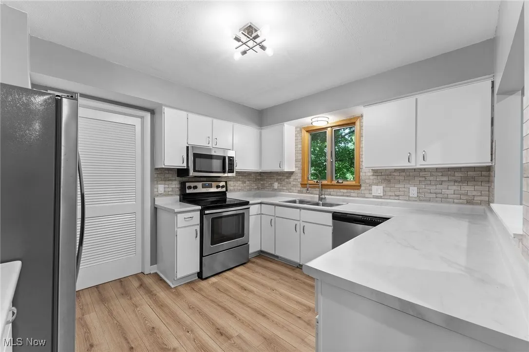 Kitchen featuring stainless steel appliances, backsplash, light countertops, white cabinetry, and light wood-style floors