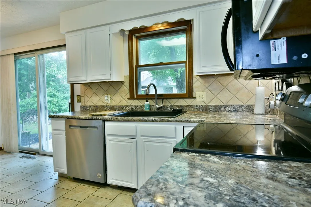 Kitchen with dishwasher, white cabinets, backsplash, and black microwave