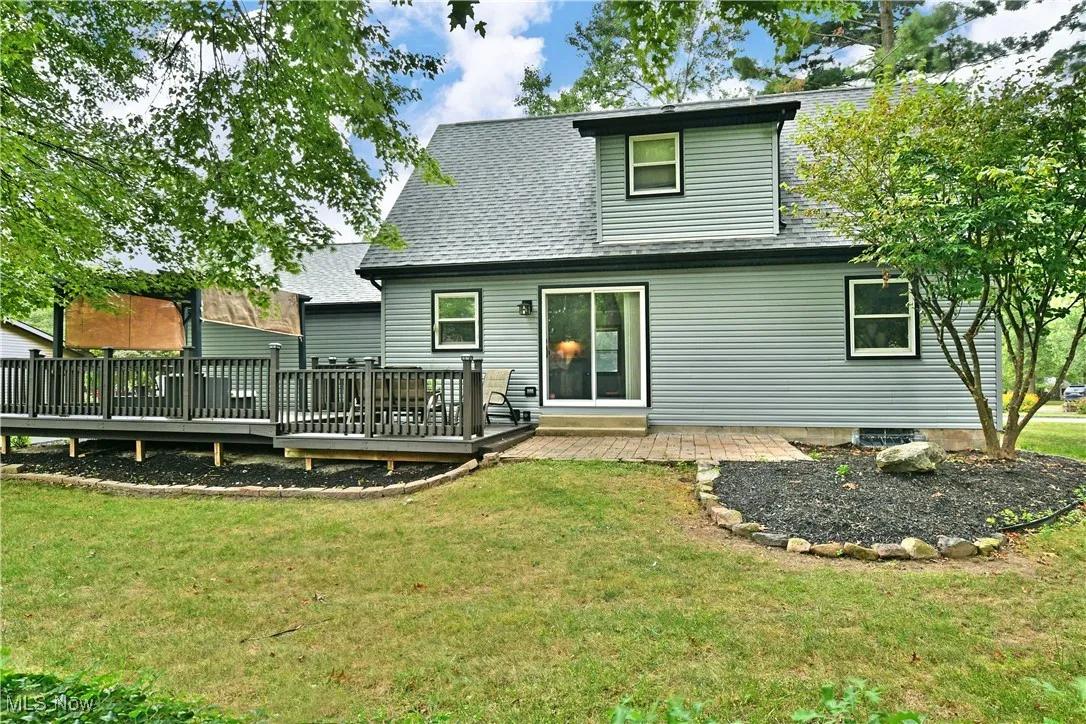 Back of property featuring roof with shingles, a lawn, and a wooden deck