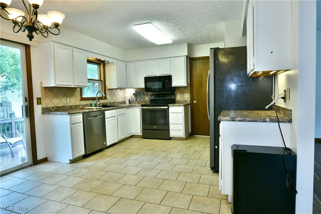 Kitchen with black appliances, tasteful backsplash, a chandelier, white cabinetry, and plenty of natural light