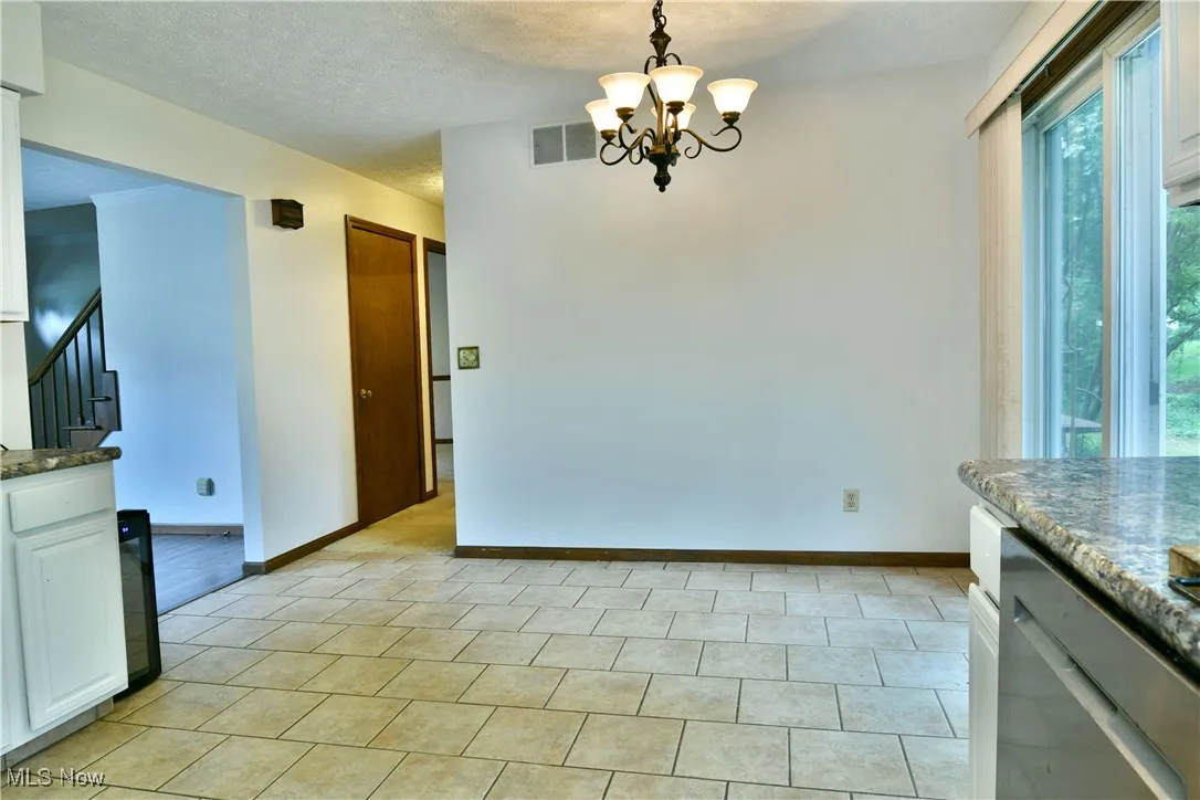 Unfurnished dining area with a chandelier, stairs, a textured ceiling, and light tile patterned flooring