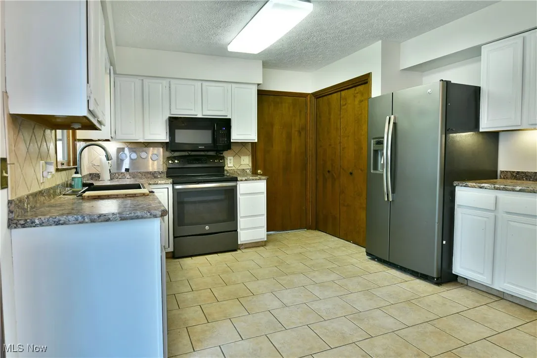 Kitchen featuring range with electric stovetop, black microwave, stainless steel fridge with ice dispenser, decorative backsplash, and white cabinets