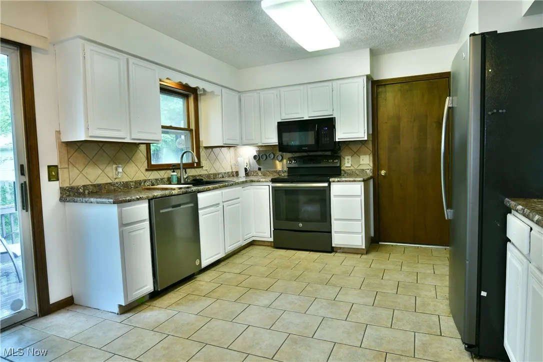 Kitchen with black appliances, dark countertops, backsplash, white cabinetry, and a textured ceiling