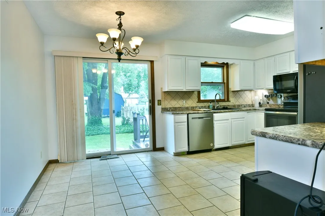 Kitchen with stainless steel appliances, backsplash, white cabinetry, a chandelier, and light tile patterned floors