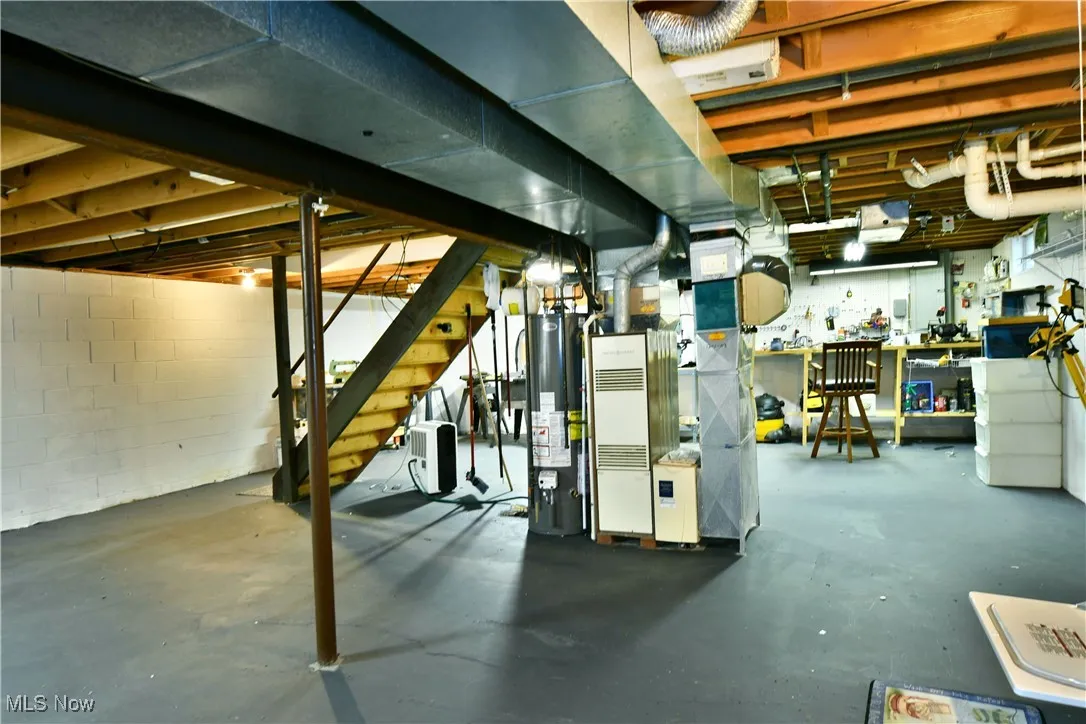 Unfinished below grade area featuring a workshop area, gas water heater, stairway, and heating unit