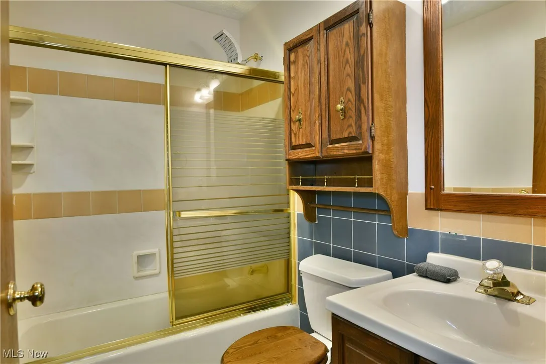 Bathroom featuring vanity, combined bath / shower with glass door, decorative backsplash, and tile walls