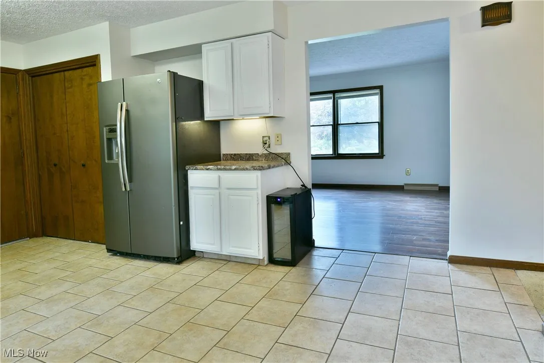 Kitchen with stainless steel fridge, a textured ceiling, white cabinets, and light tile patterned flooring