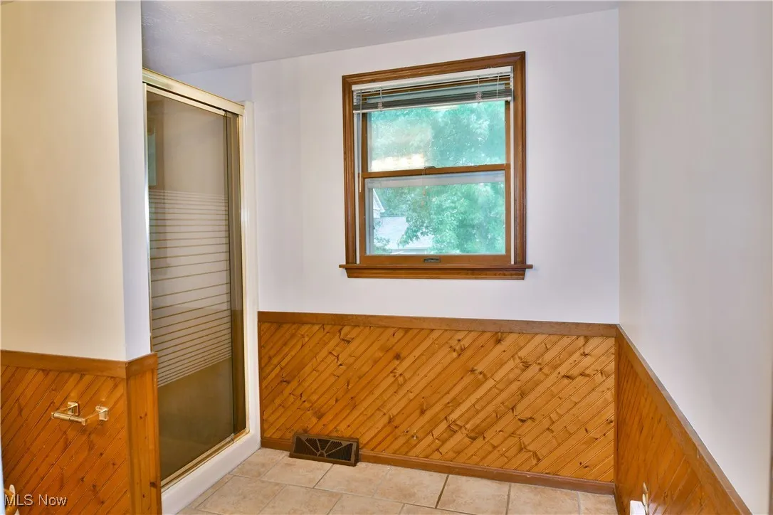 Bathroom featuring wainscoting, wooden walls, a shower stall, and tile patterned flooring
