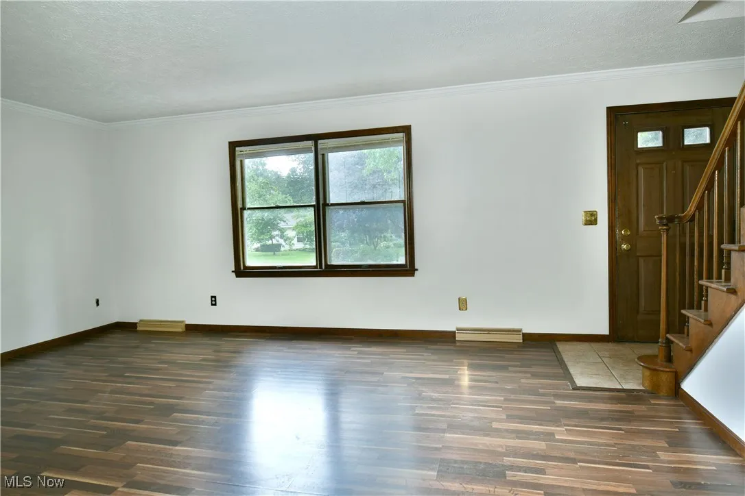 Spare room featuring wood finished floors, stairs, ornamental molding, and a textured ceiling
