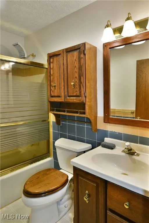 Bathroom with tile walls, vanity, enclosed tub / shower combo, and a textured ceiling