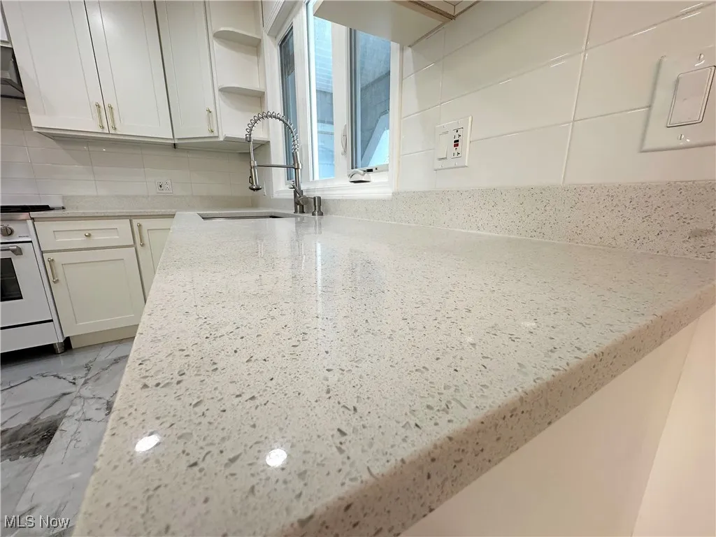 Kitchen with white stove, backsplash, open shelves, and light granite countertops