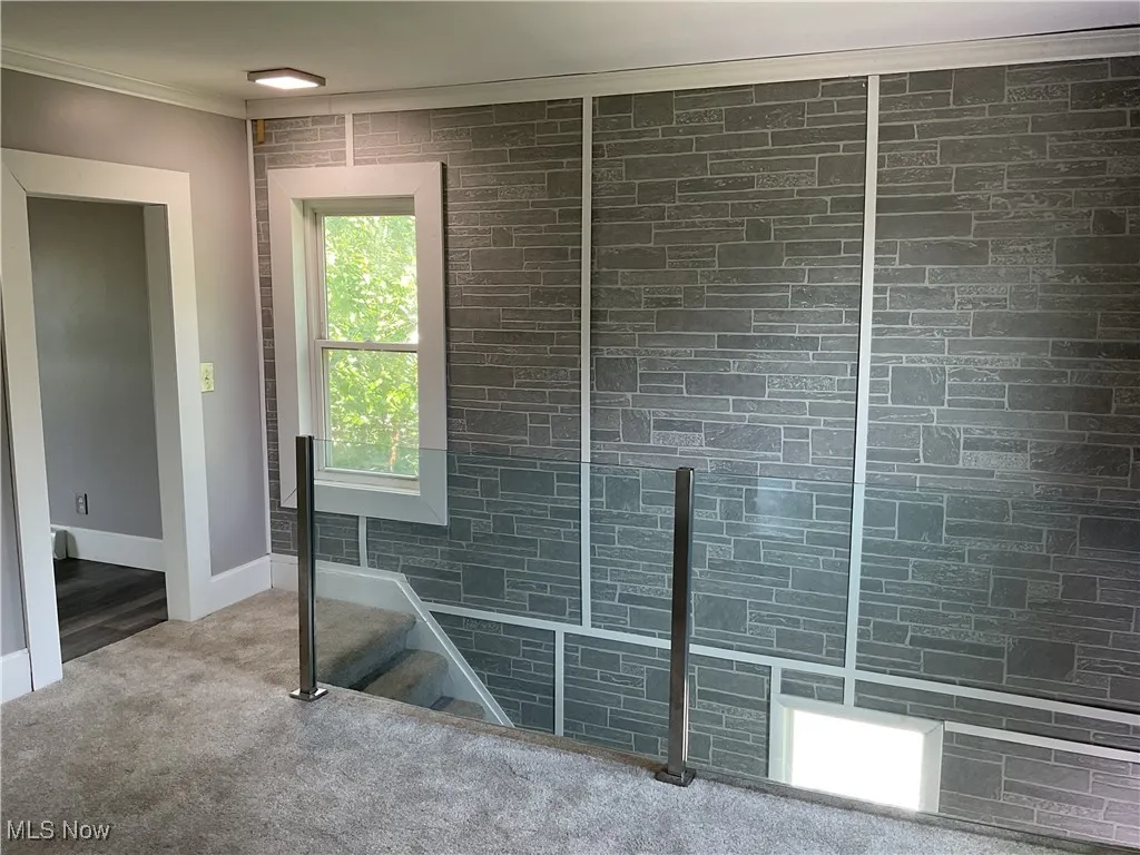 Stairway leading to the carpeted bonus room featuring a brick style accent wall l