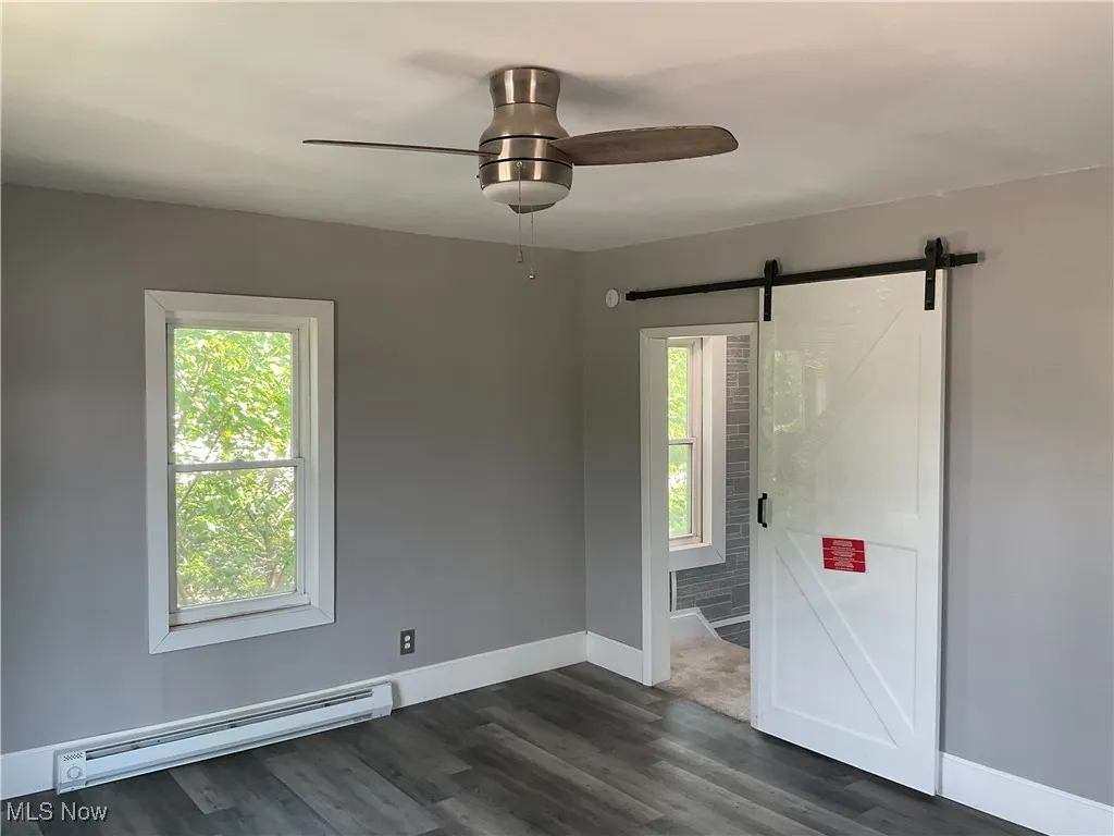 Bedroom #1 featuring a baseboard radiator, a barn door, plenty of natural light, and a ceiling fan