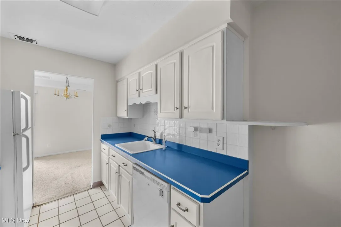 Kitchen featuring white appliances, white cabinetry, decorative backsplash, light tile patterned floors