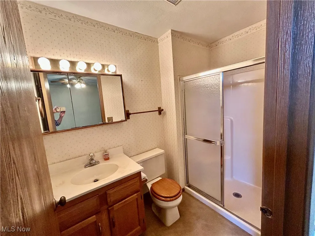 Bathroom featuring wallpapered walls, a shower stall, vanity, and ceiling fan