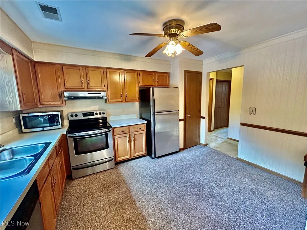 Kitchen with stainless steel appliances , ceiling fan, brown cabinets, light countertops, and ornamental molding