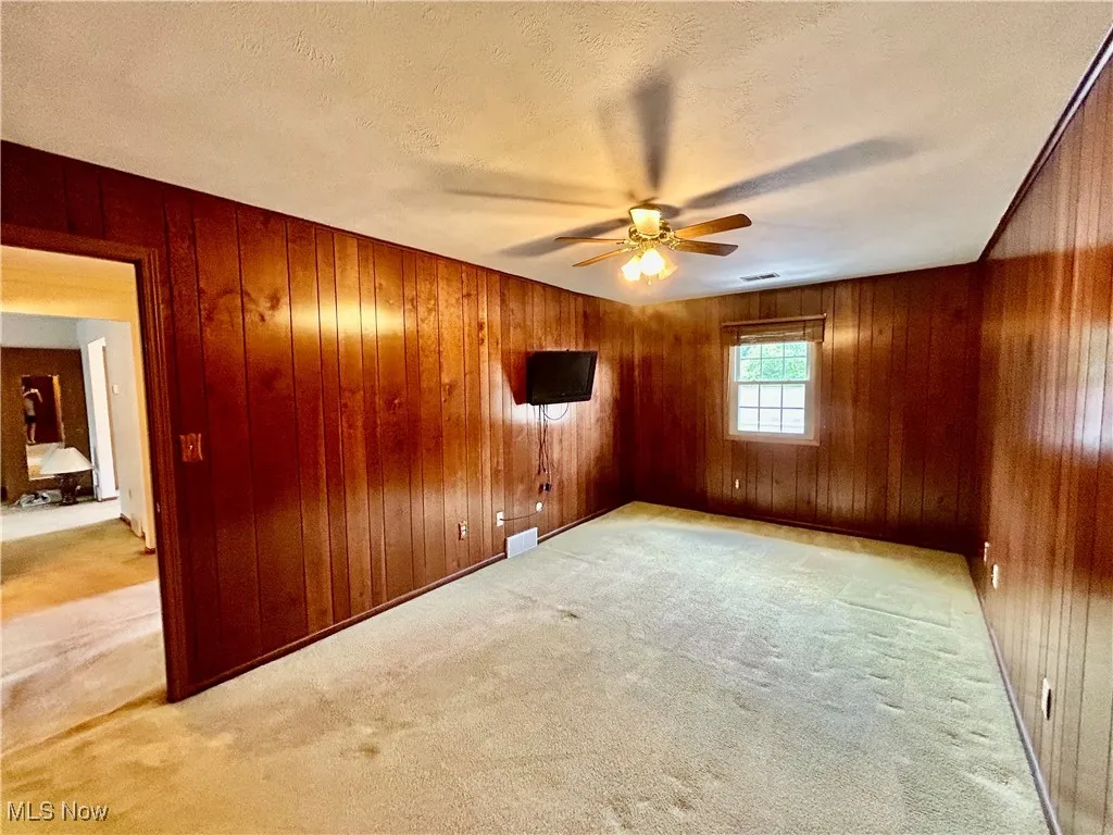 Bedroom with carpet, a ceiling fan, wood paneled walls, and a wall mounted tv