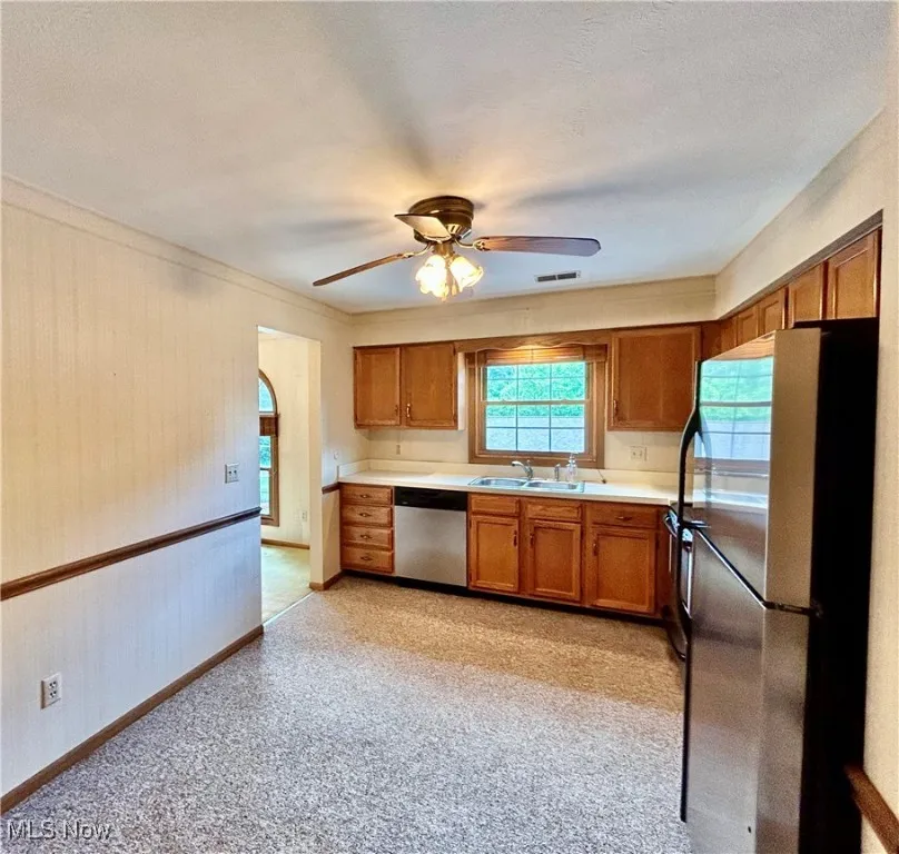 Kitchen featuring stainless steel appliances, brown cabinetry, a ceiling fan, and light countertops